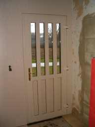 Voordeur van binnenaf met 4 verticale stijlen en 1 horizontale stijl voor de scheiding tussen glas boven en paneel onder. Messing deur kruk