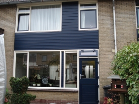 Achtergevel voorzien van kunststof kozijnen in kleur creme met de draaiende delen donkerblauw ral 5011. Het middenpaneel voorzien van keralit gevelpanelen. De achterdeur als boerendeur in 2 delen te openen.