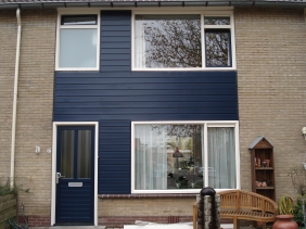 Voorgevel voorzien van kunststof kozijnen in kleur creme met de draaiende delen donkerblauw ral 5011. Het middenpaneel voorzien van keralit gevelpanelen. De voordeur met massief onderdorpel